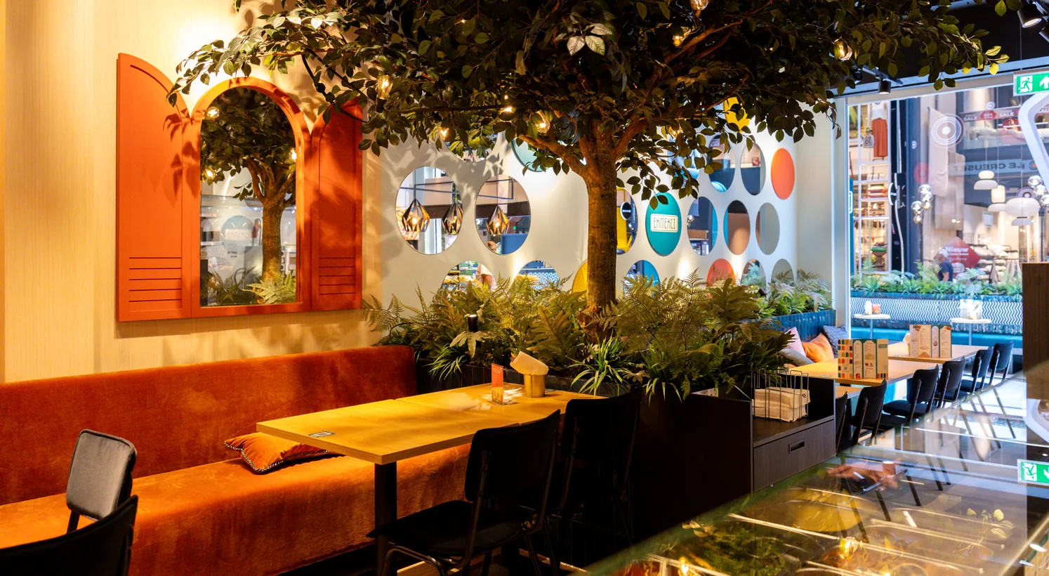 Het interieur van Ekmekci met een grote boom vol lichtjes, oranje luiken rond een spiegel en een oranje fluwelen bank
