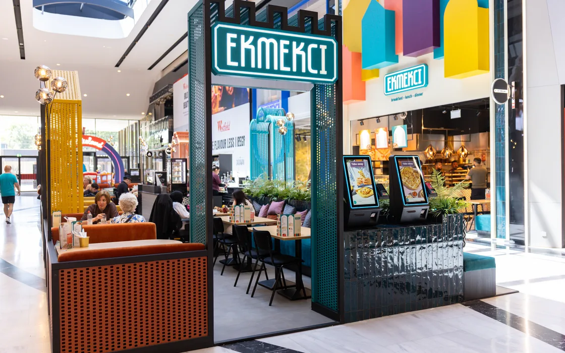 Een Ekmekci-vestiging in een overdekt winkelcentrum, met het verlichte EKMEKCI-bord boven de petrolkleurige ingang en gasten aan tafel