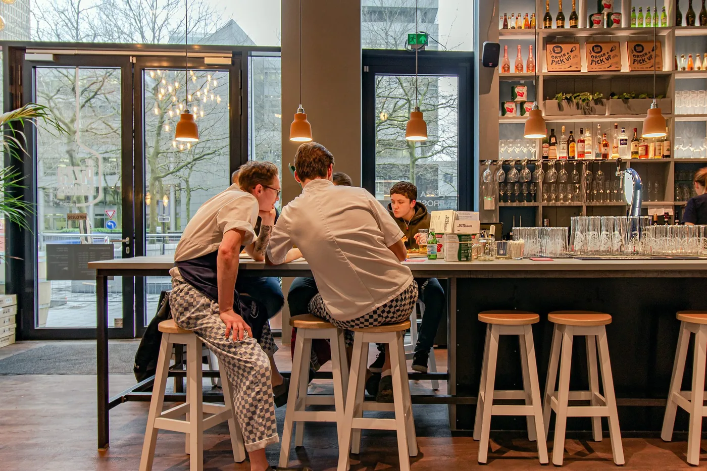 Medewerkers van De Pizzabakkers aan de bar in de avond