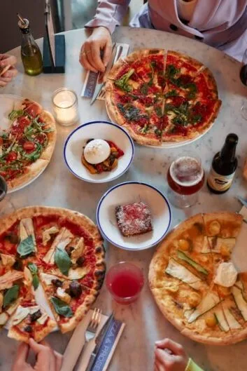Een gedekte tafel vol pizza's, burrata en een biertje bij De Pizzabakkers