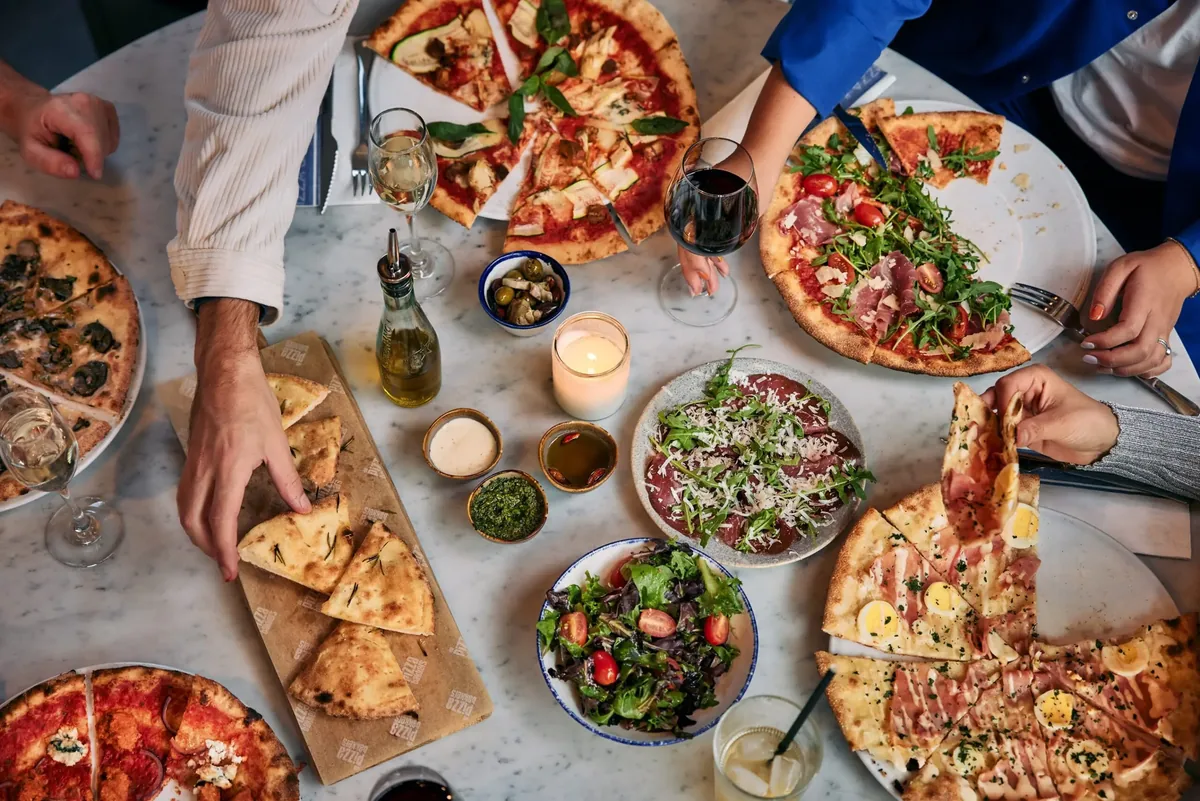 Een tafel vol gedeelde pizza's bij De Pizzabakkers