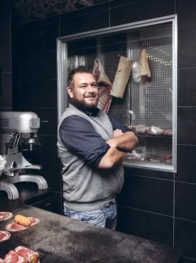 Een slager van Vleeschmeester poseert voor de vitrine met vlees